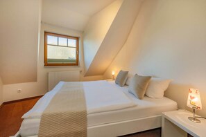 A bedroom with a bed, a nightstand, a lamp, a window, and a radiator.
