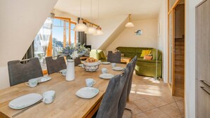 A dining area with a wooden table, chairs, and a green sofa in the background. - Modern vacation apartment with garden, sauna & whirlpool - ideal for families (Loddin)