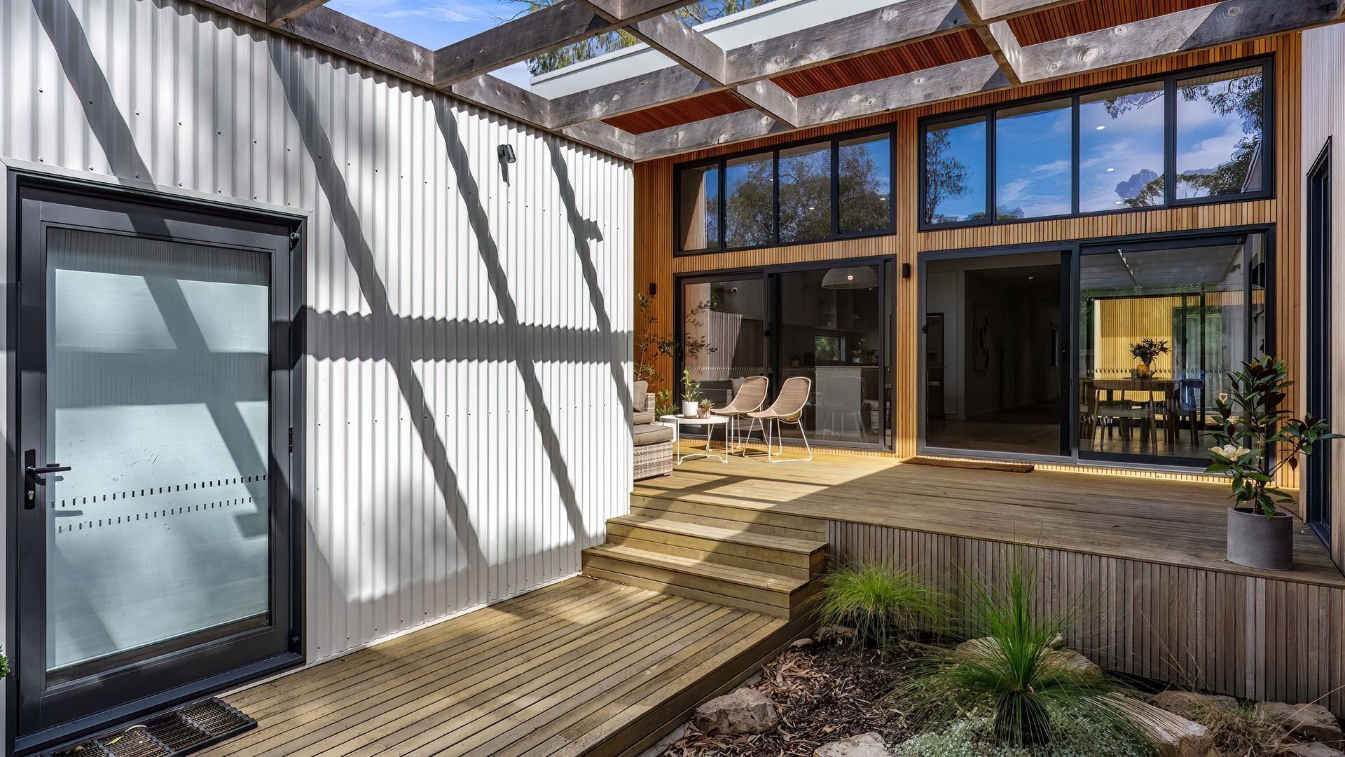 A modern house with a wooden deck, large windows, and a sliding glass door.