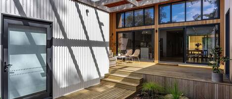 A modern house with a wooden deck, large windows, and a sliding glass door.