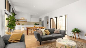 A modern living room with a grey sofa, a wooden dining table, and a kitchen in the background.