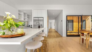 A modern kitchen with white cabinetry, a central island with stools, and a dining area with a wooden table and chairs.