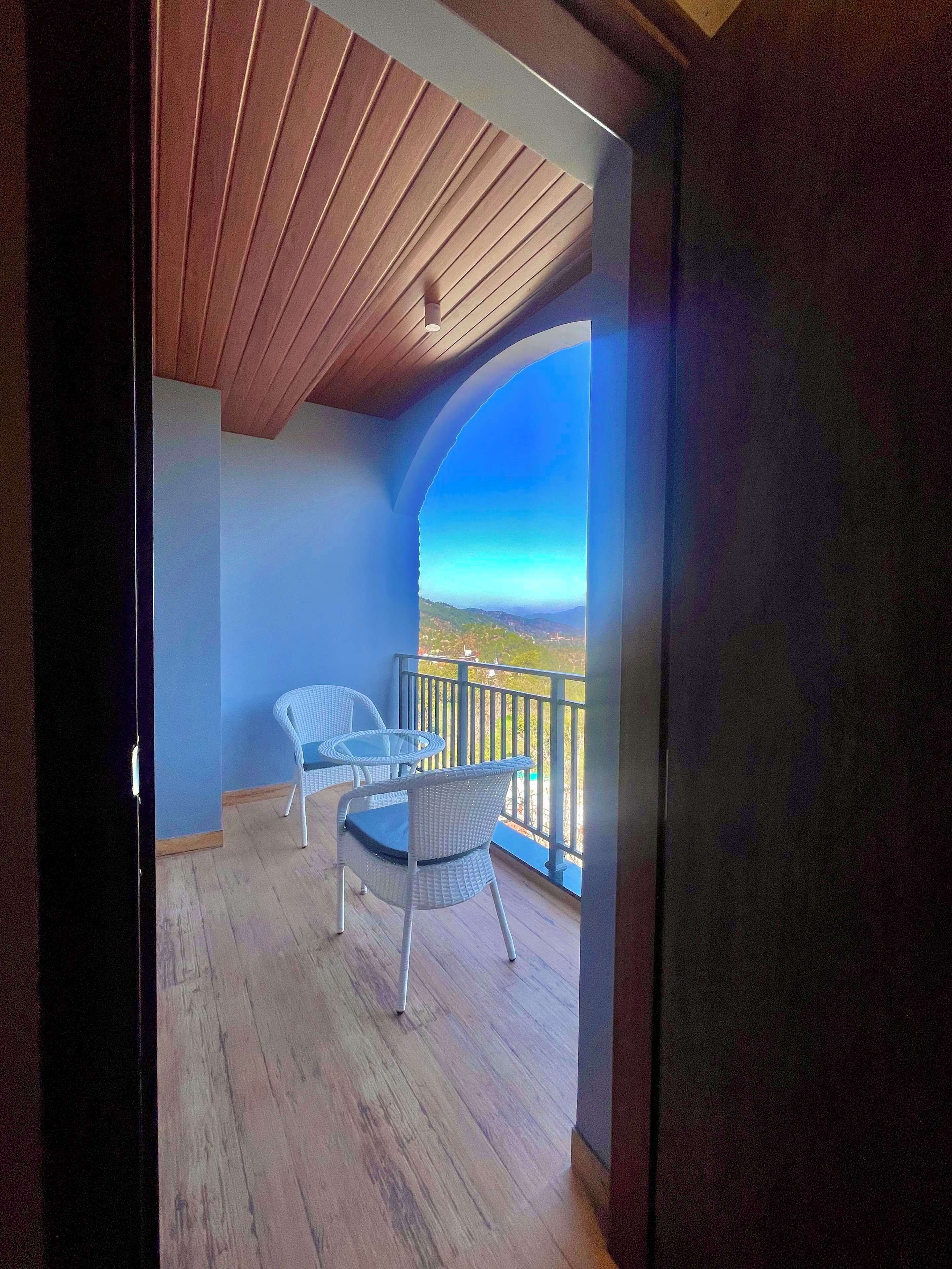 A balcony with two wicker chairs, a wooden floor, and a view of the landscape.