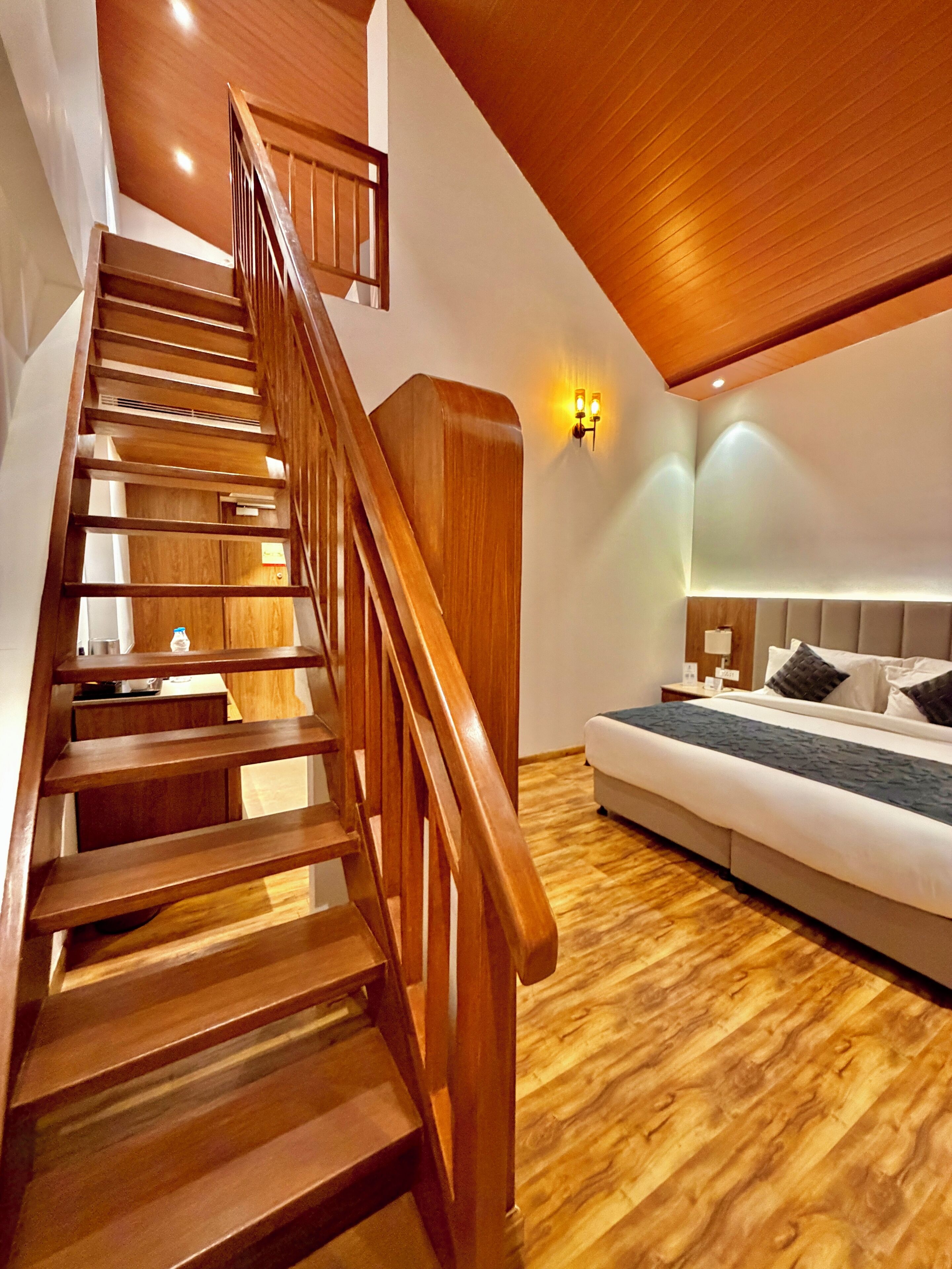 A wooden staircase leading to a bedroom with a bed and a nightstand.