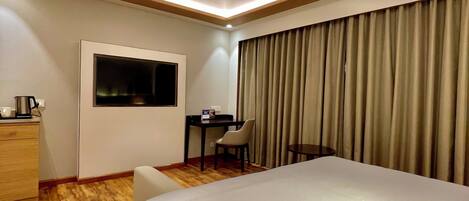 A hotel room with a large bed, a desk with a chair, a TV mounted on the wall, and a ceiling fan.
