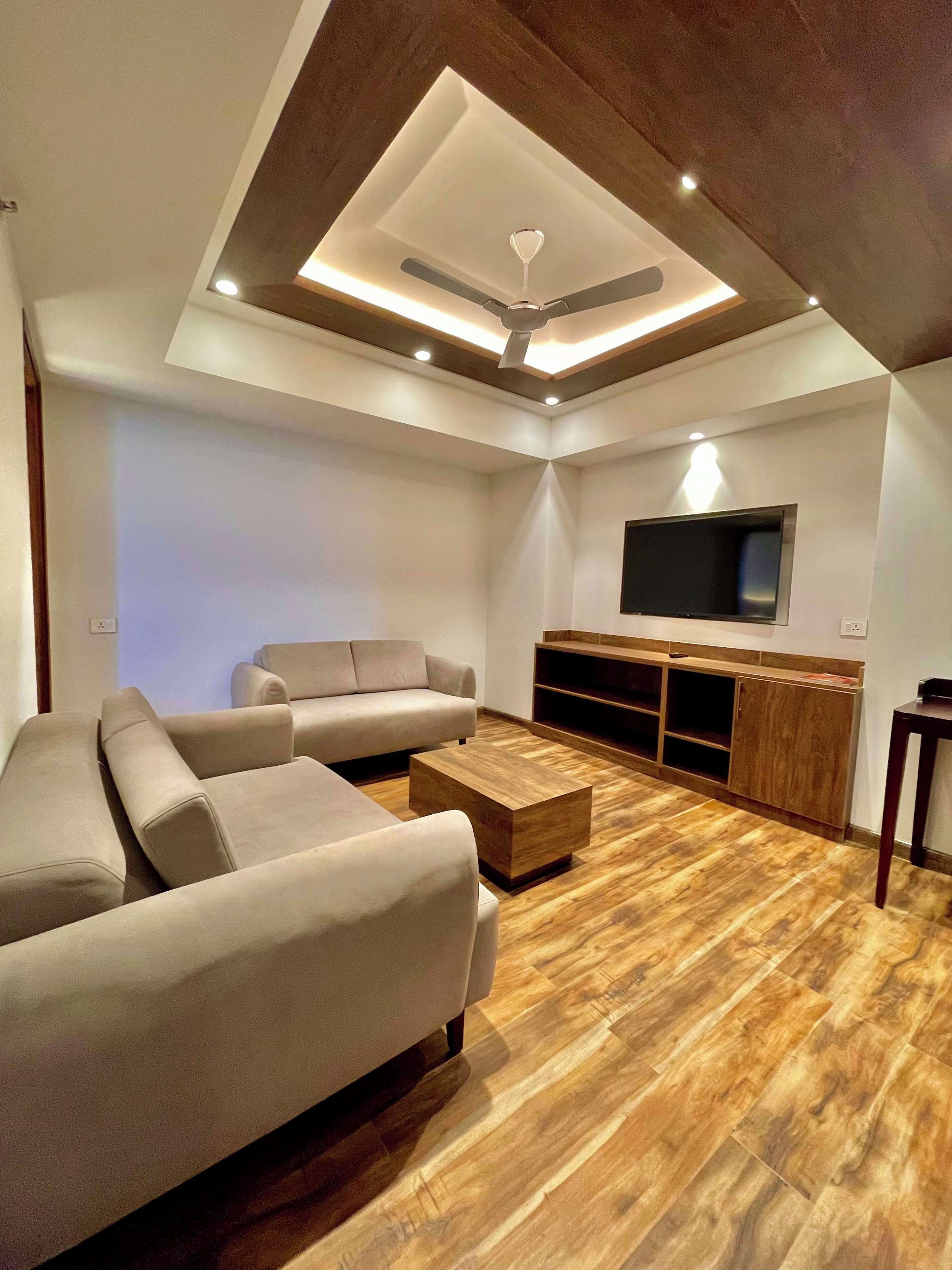Una sala de estar moderna con un sofá modular, una mesa de centro, piso de madera, iluminación empotrada en el techo y un televisor de pantalla plana montado en la pared.