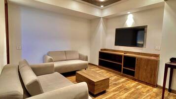 Una sala de estar moderna con un sofá modular, una mesa de centro, piso de madera, iluminación empotrada en el techo y un televisor de pantalla plana montado en la pared.
