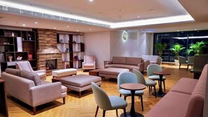 Un espace de détente moderne, doté de canapés, de fauteuils et de tables, avec une cheminée et des étagères où sont exposés des objets décoratifs.