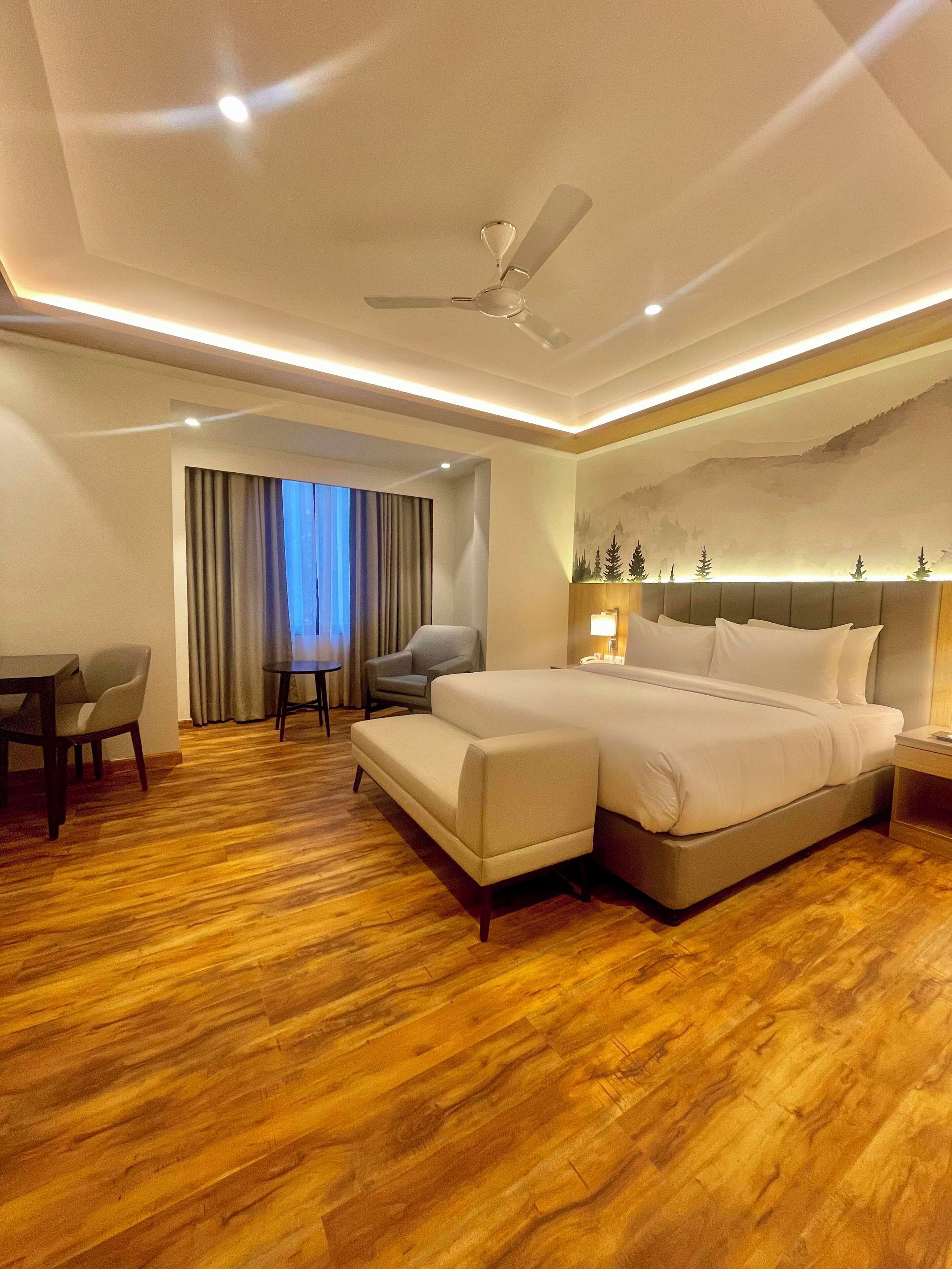 A hotel room with a large bed, a desk, a chair, and a ceiling fan.