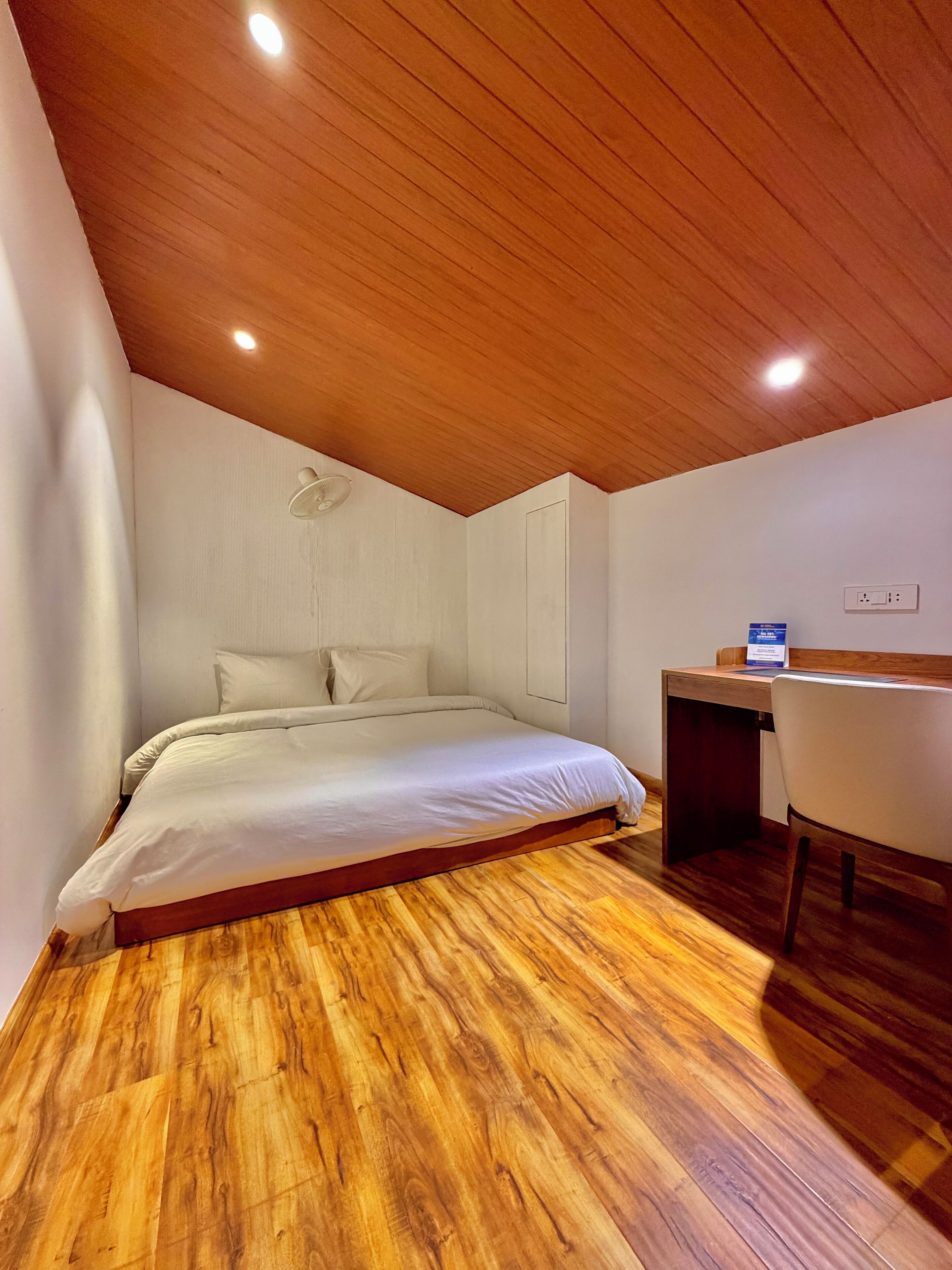 A bedroom with a wooden ceiling, a bed, a desk, and a chair.