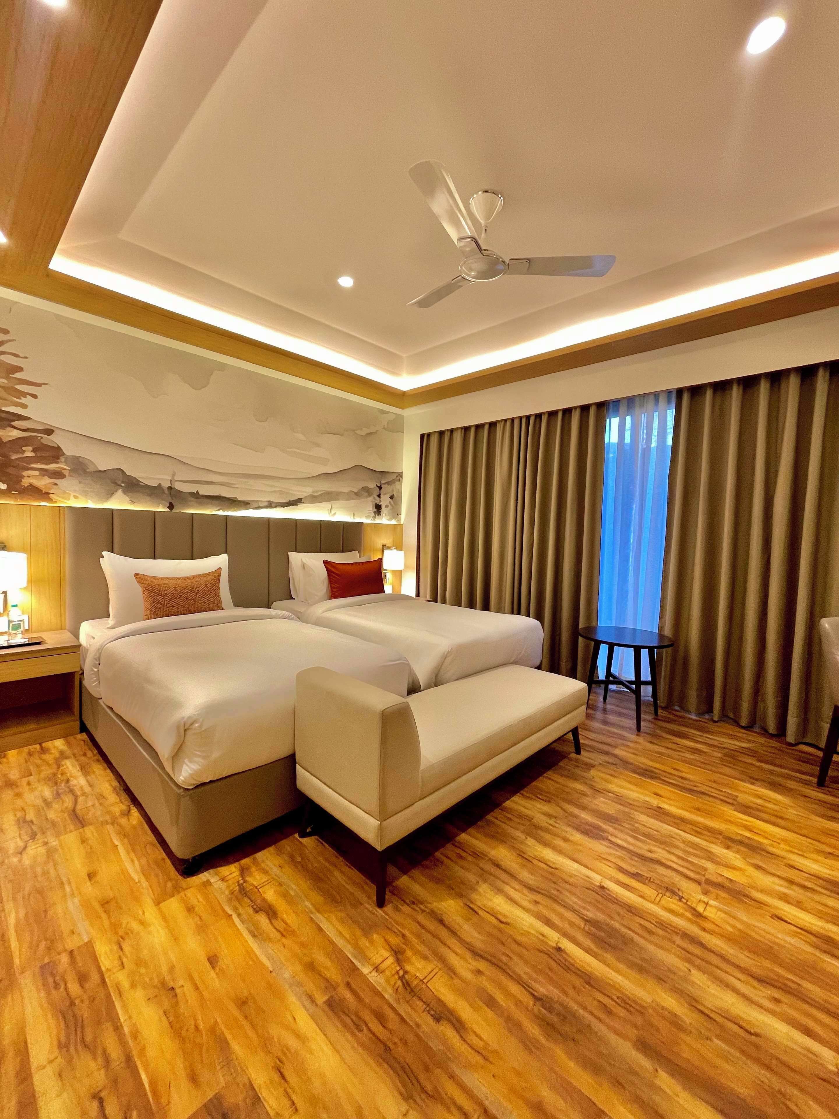 A hotel room with a large bed, a sofa, a ceiling fan, and a view of the outdoors through the window.
