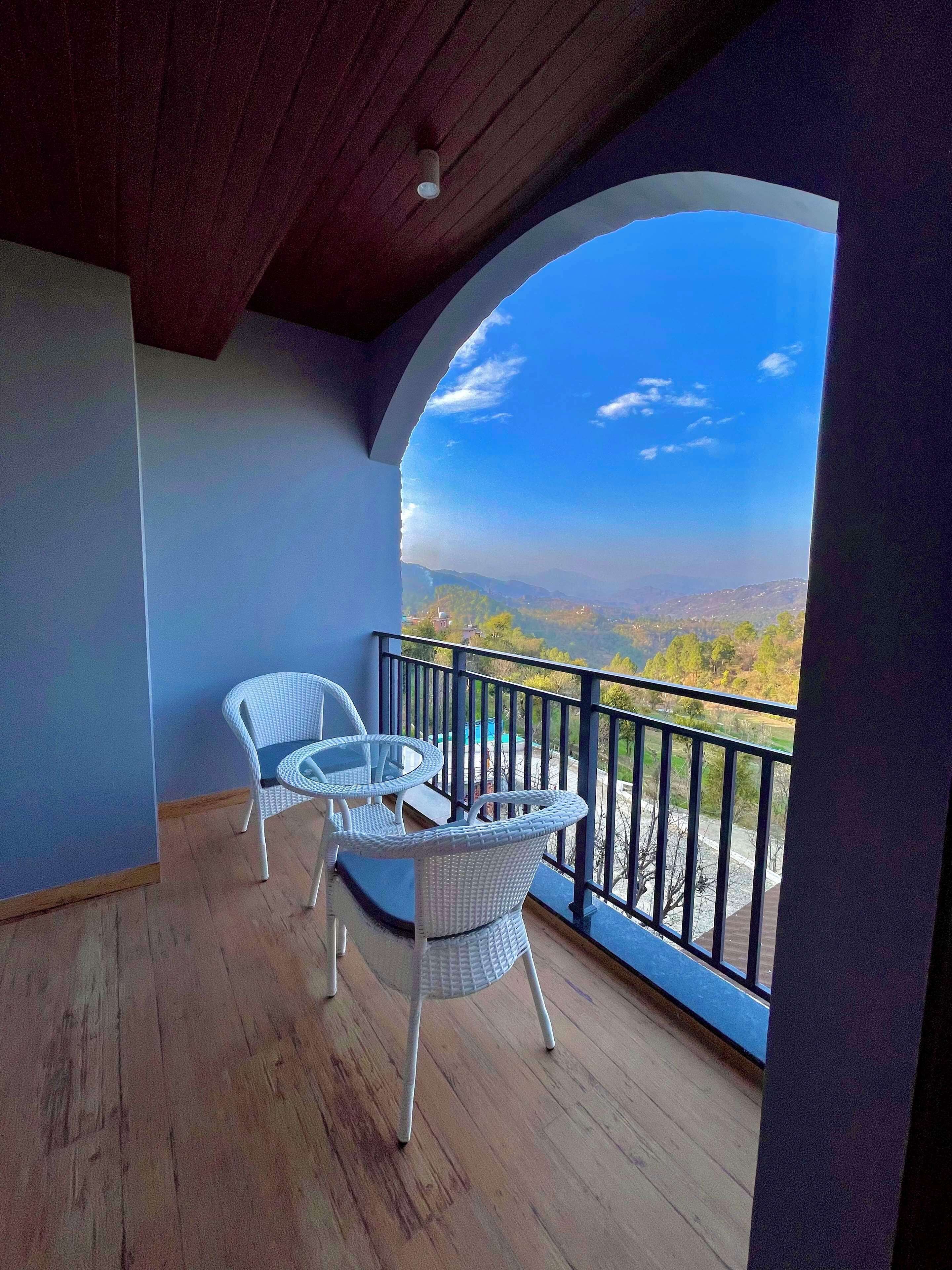 Un balcon avec deux fauteuils en osier et une table en verre, offrant une vue sur un paysage magnifique.