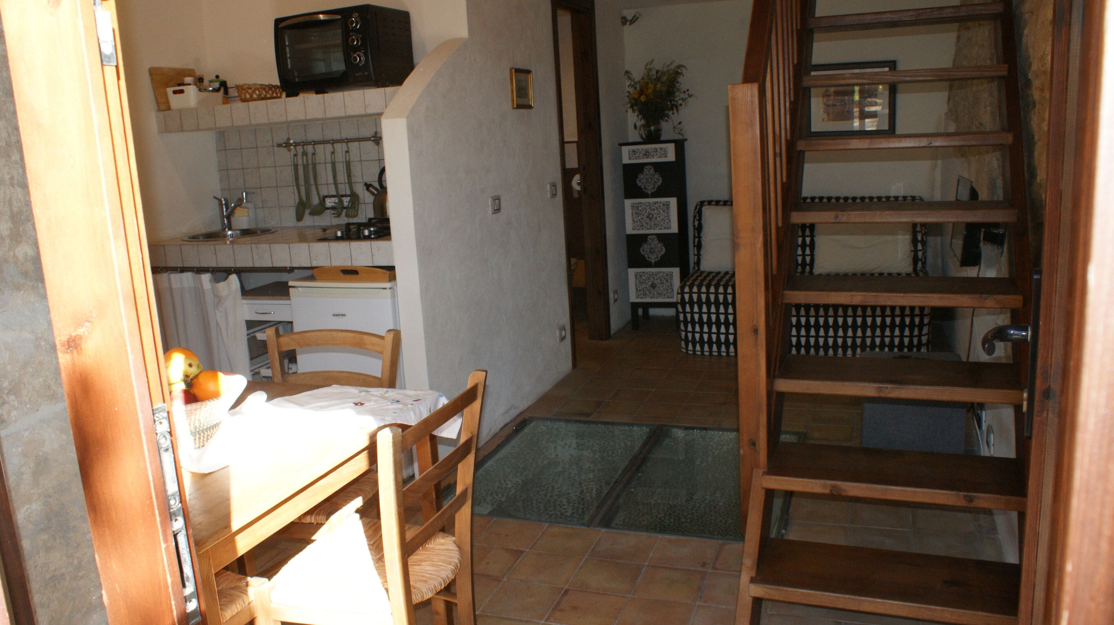 A kitchen with a microwave, a sink, and a refrigerator. There is a dining table with chairs and a small rug. A wooden ladder is leaning against the wall.
