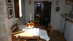 Een eetgedeelte met een tafel gedekt voor twee personen, een fruitschaal en een kast met glazen deuren.