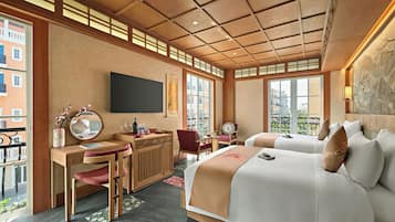 Quarto de hotel com escrivaninha de madeira, duas camas, uma janela ampla e vista para edifícios.