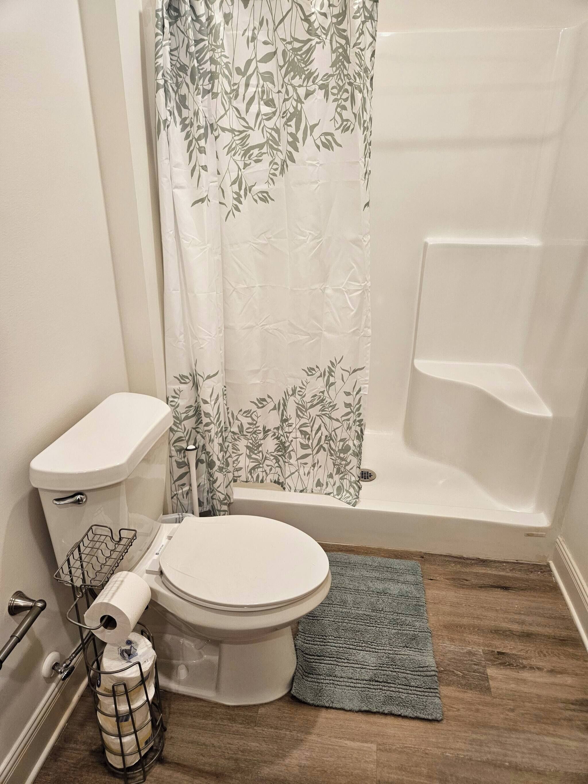 A bathroom with a toilet, shower, and a small rug.