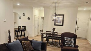 A living room with a dark brown sofa, a patterned rug, a wooden coffee table, and a dining area with a chandelier. - Madison Cozy House for Comfort and Relaxation (Madison)