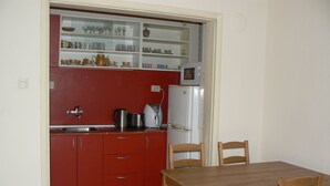 Una cocina compacta con armarios rojos, un refrigerador blanco y una mesa de comedor de madera con sillas.
