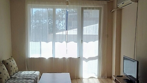 Una sala de estar con un sofá, una mesa de centro, un televisor sobre un mueble bajo y una ventana con cortinas.