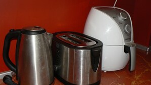 Una tetera de acero inoxidable, un tostador y una tetera eléctrica blanca sobre una encimera de mármol.