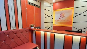 Een receptiebalie met een bordje waarop 'ENRICH HOTEL' staat en een rode, beklede zitbank.