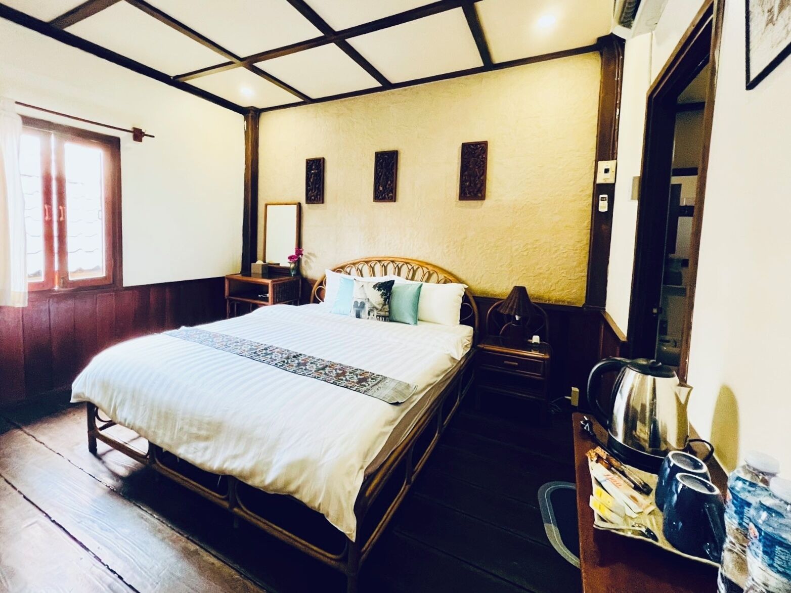 Une chambre à coucher avec un lit en bois, une table de chevet, un miroir et une fenêtre avec des rideaux.