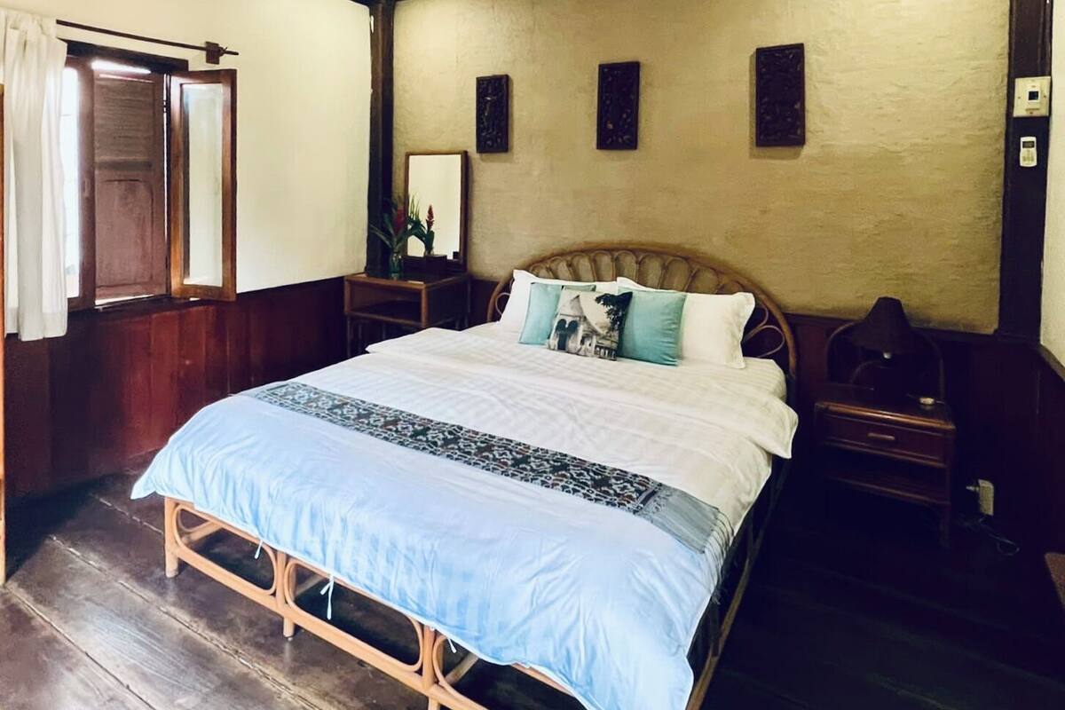 Quarto com cama de madeira, mesa de cabeceira e luminária fixada na parede.