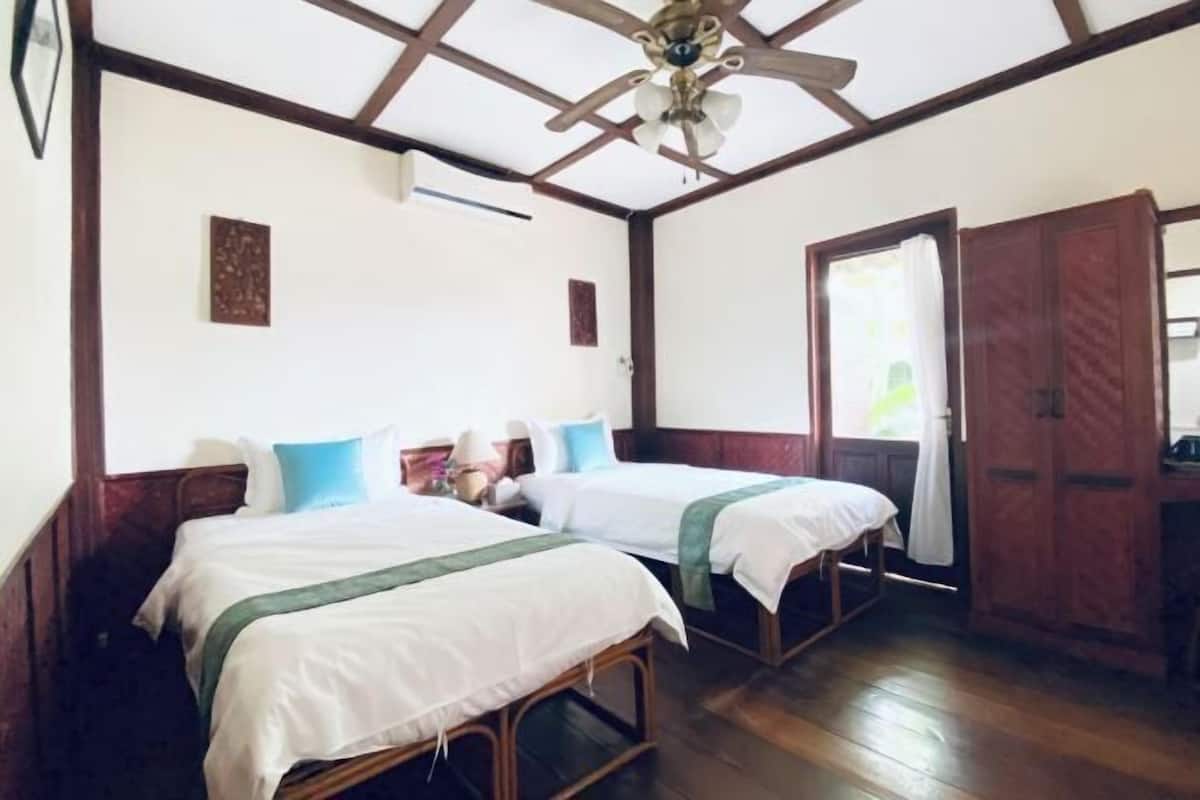 Quarto com duas camas, piso de madeira, ventilador de teto e guarda-roupa.