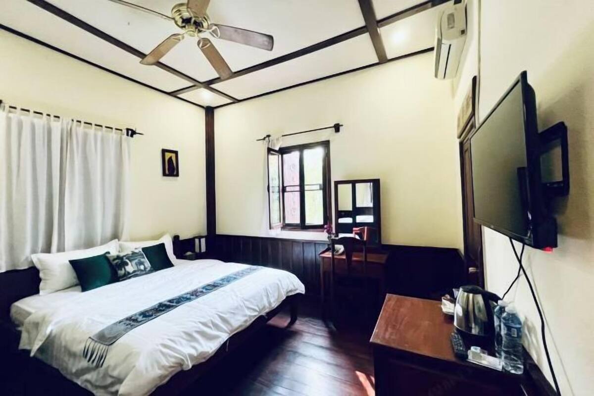 Quarto com cama, escrivaninha, cadeira, televisão e ventoinha no teto.