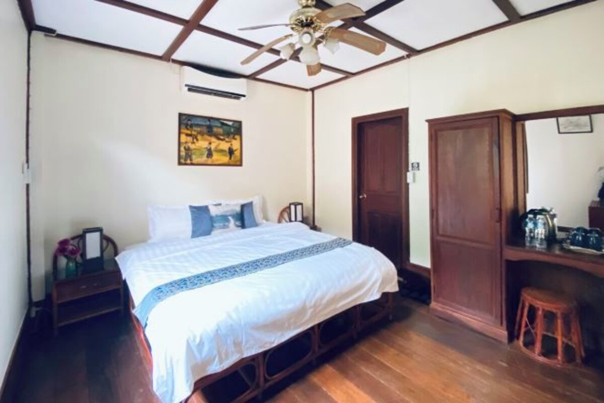 A bedroom with a bed, wooden furniture, a ceiling fan, and a painting on the wall.