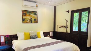 A hotel room with a large bed, a painting on the wall, a window with a view of greenery, and a wooden floor. - Villa de Mekong (Vientiane)