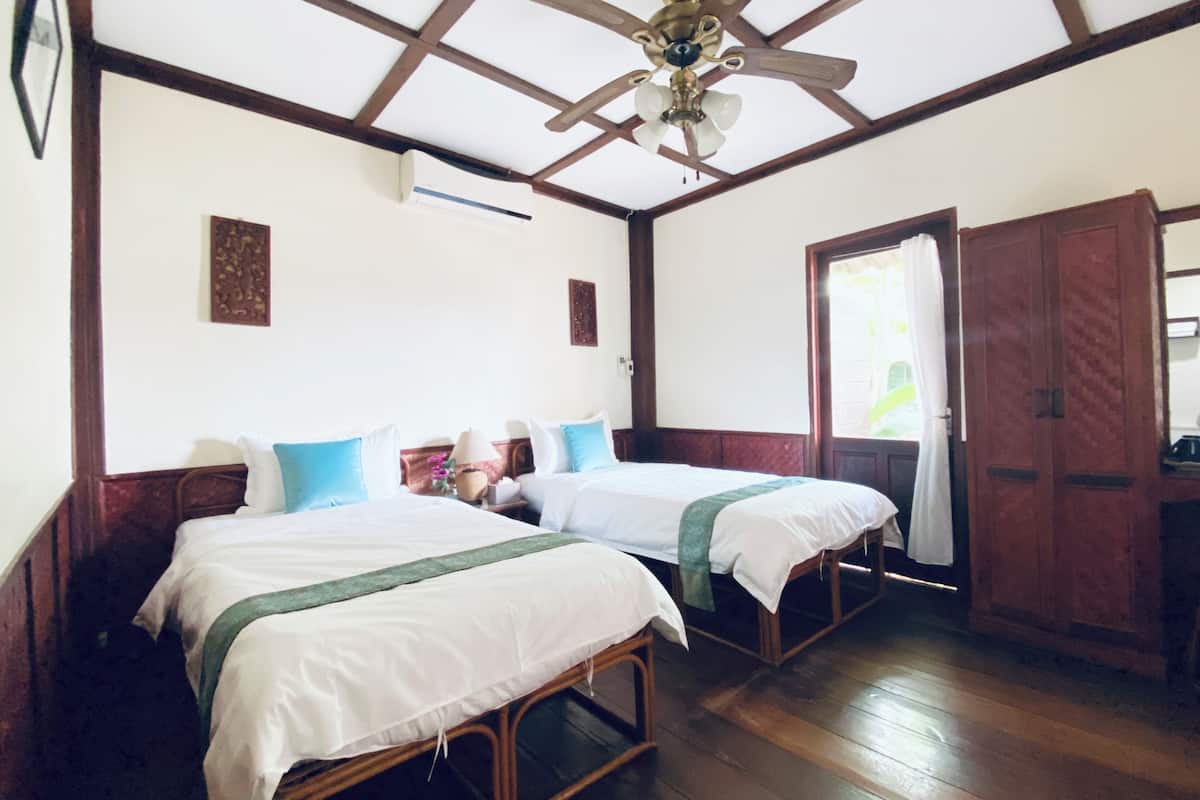 Quarto com duas camas, piso de madeira, ventoinha no teto e guarda-roupa.
