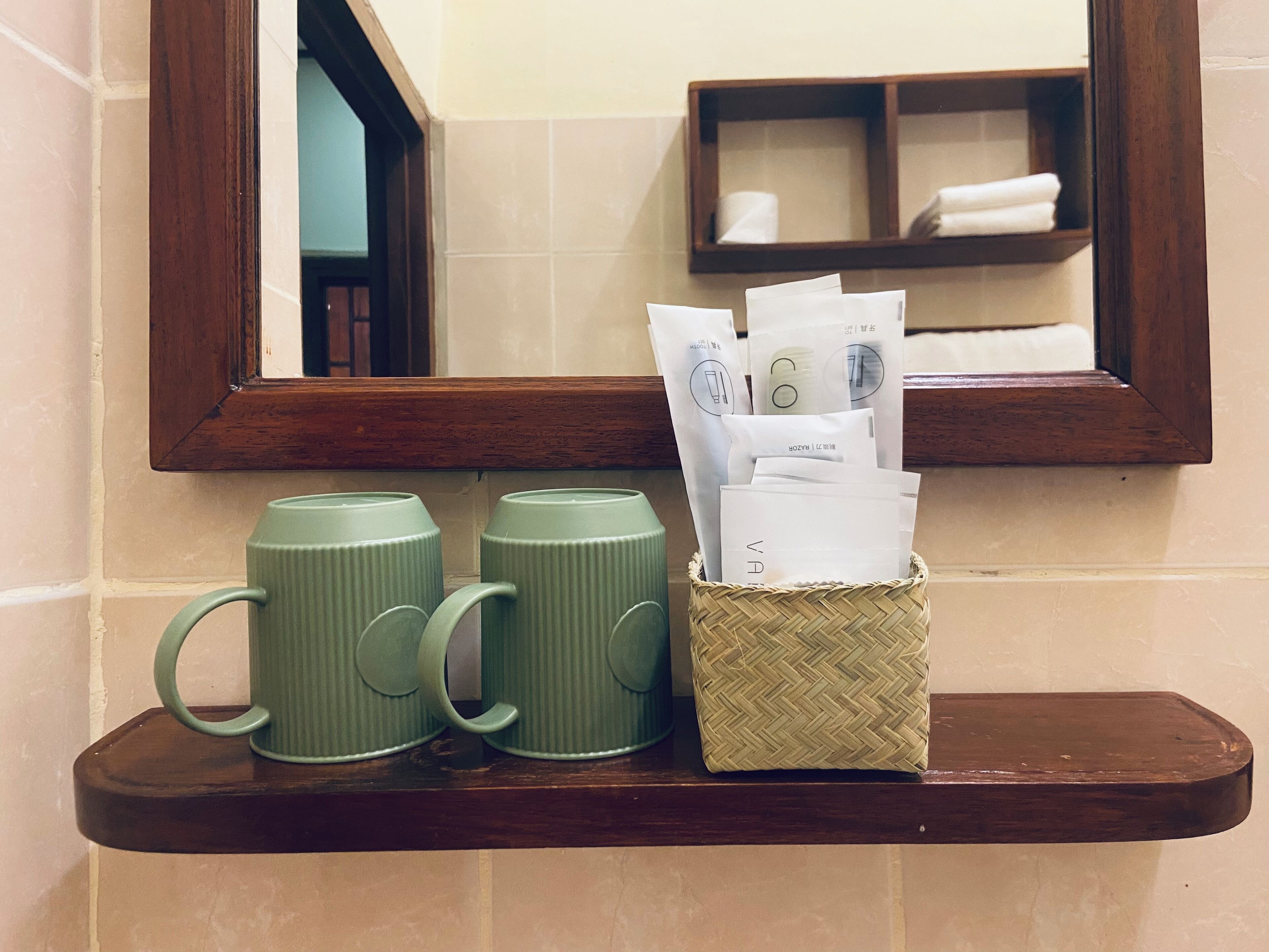Un estante de baño con dos tazas verdes y una cesta de mimbre con artículos de aseo.