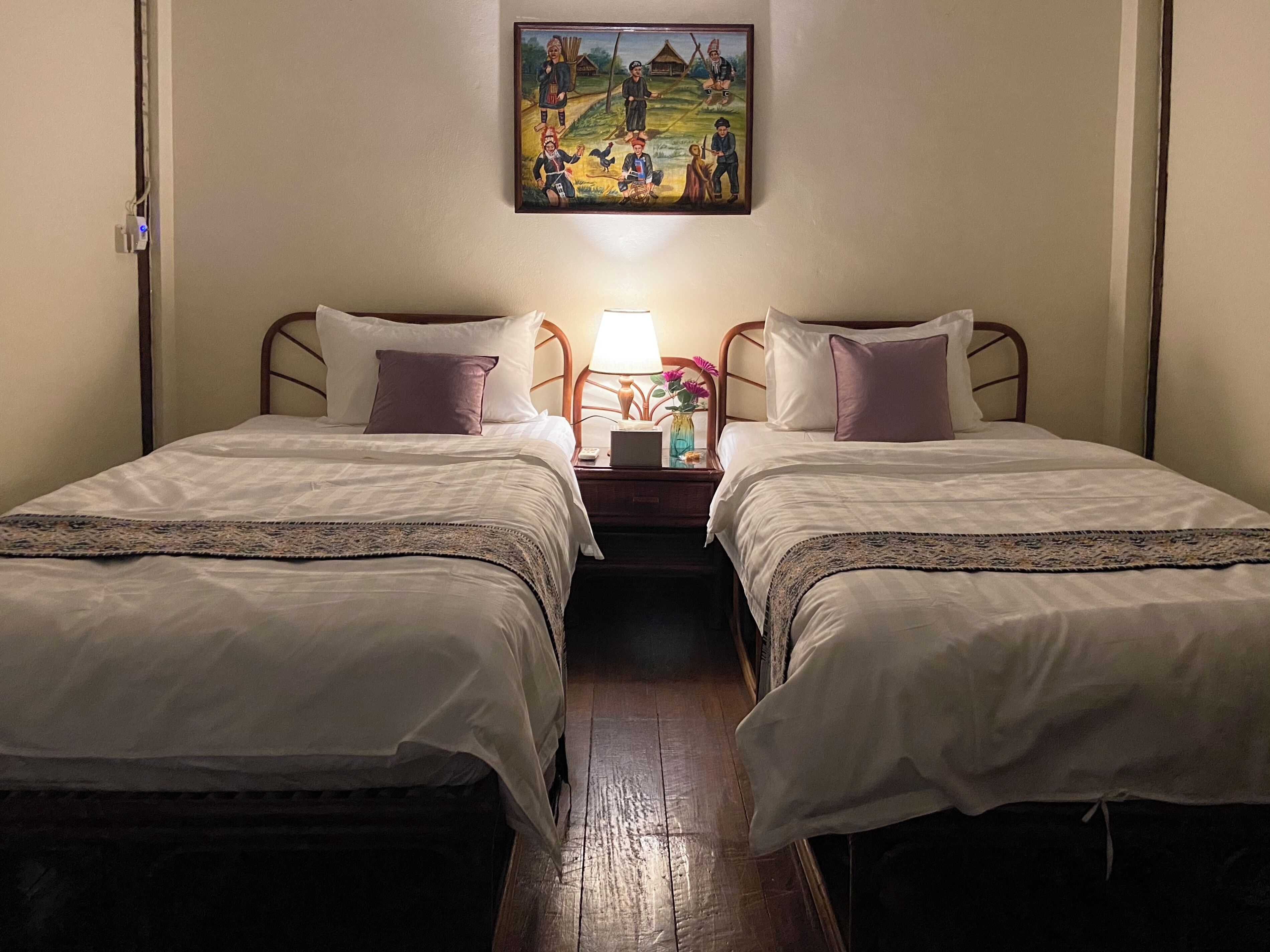 Una habitación con dos camas individuales, una mesita de noche con lámpara y un cuadro en la pared.