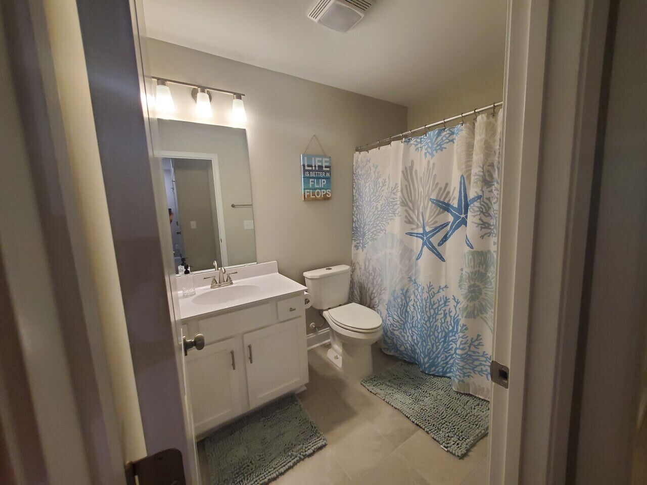 A bathroom with a white sink, mirror, and toilet. There is a shower curtain with a starfish design.