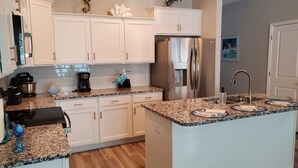 Eine moderne Küche mit weißen Schränken, Granit-Arbeitsplatten, einem Edelstahl-Kühlschrank und einer integrierten Kochinsel mit Spüle.