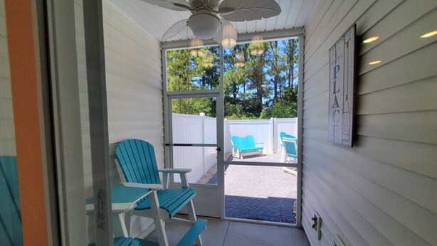 Eine überdachte Veranda mit Deckenventilator, zwei blaue Stühle und Blick auf einen Hinterhof mit weißem Zaun und Bäumen.