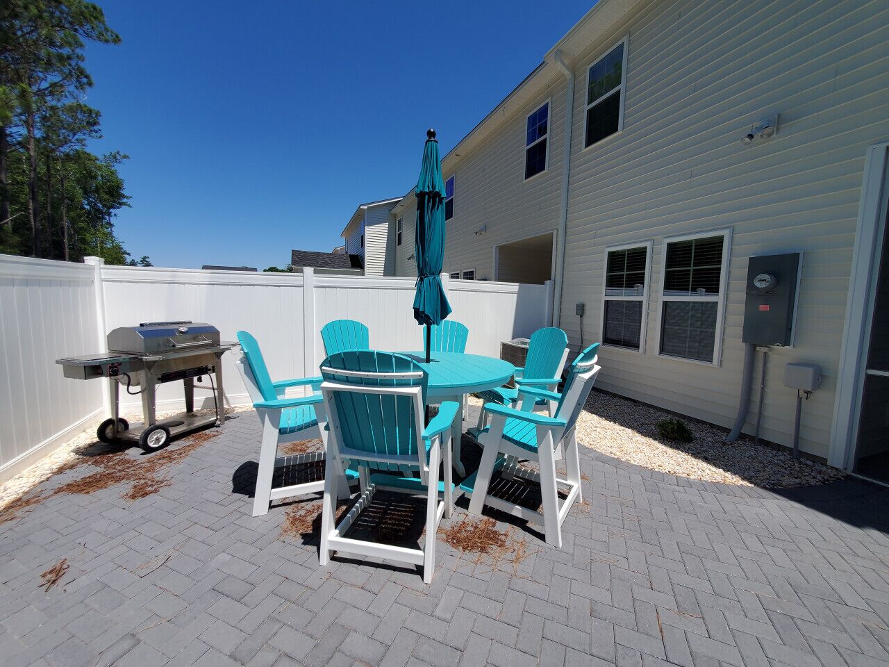 An outdoor patio with a white fence, a grill, and turquoise chairs.
