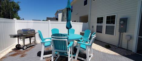 An outdoor patio with a white fence, a grill, and turquoise chairs.