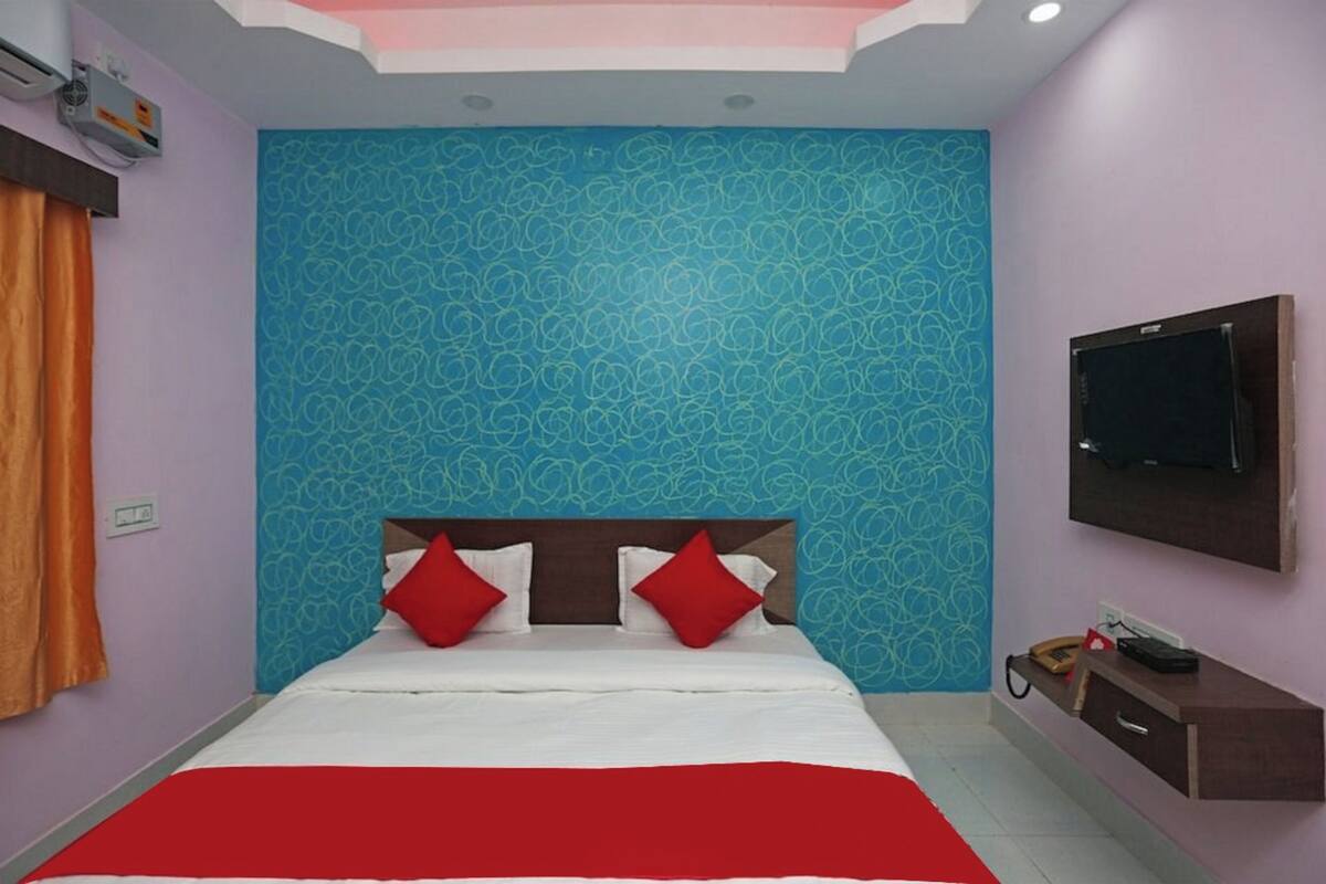 A hotel room with a bed, a TV mounted on the wall, and a small desk with a telephone.