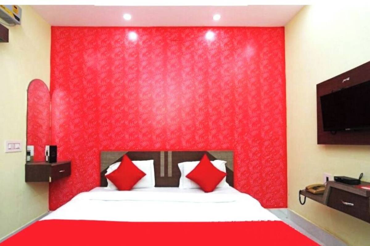 A hotel room with a large bed, red walls, a TV mounted on the wall, and a bedside table with a phone.