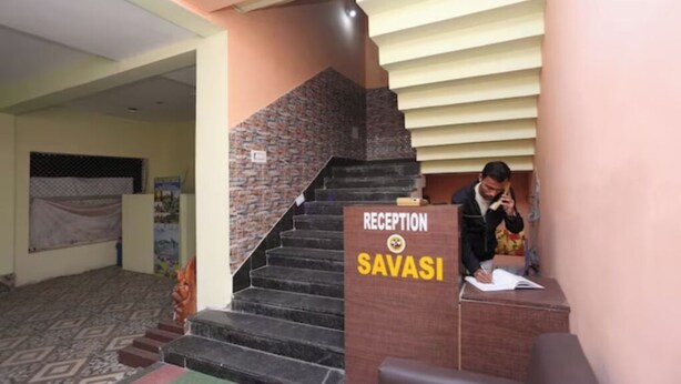 A reception area with a staircase leading to upper floors, a reception desk labeled "RECEPTION SAVASI," and a person seated at the desk. - DhamStay Hotel Savashi Near Temple Puri (Puri)