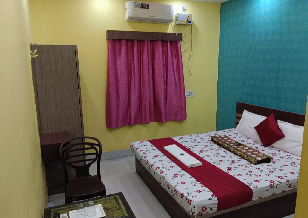 A bedroom with a bed, a chair, a desk, and an air conditioning unit.