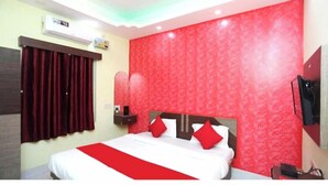 A hotel room with a bed, red curtains, a red patterned wall, and a mounted TV. - DhamStay Hotel Savashi Near Temple Puri (Puri)