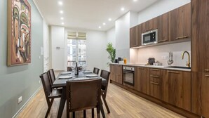 A modern kitchen with wooden cabinets, a microwave, and a dining area with a table set for four. - 21.#Opera#Louvre#Paris02#2bedrooms#AC (Paris)