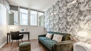 Uma sala de estar moderna com um sofá verde, uma poltrona preta, um banquinho pequeno e uma mesa de escritório com uma luminária.
