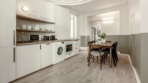 Cozinha moderna com armários brancos, máquina de lavar embutida e área de jantar com mesa e cadeiras de madeira.