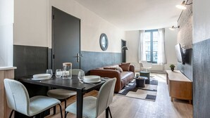 Un salon moderne avec un canapé, une table basse et un coin repas comprenant des chaises et une table dressée pour deux personnes.