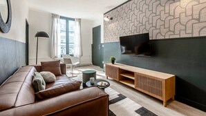 Un salon moderne avec un canapé en cuir marron, un meuble TV en bois et un mur orné d’un motif.