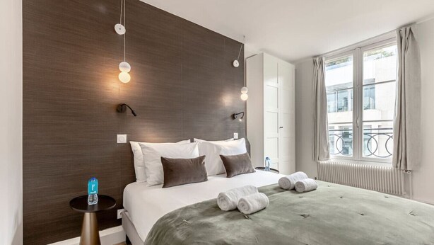 Une chambre moderne avec un grand lit, des lampes de chevet et une vue sur la ville par la fenêtre.